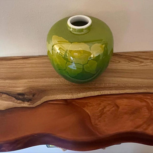 Green ceramic vase with floral design on a wooden surface