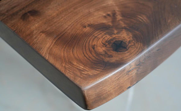 Close-up of a rustic wooden tabletop corner showing rich brown wood grain, natural knots, and a smooth polished finish.