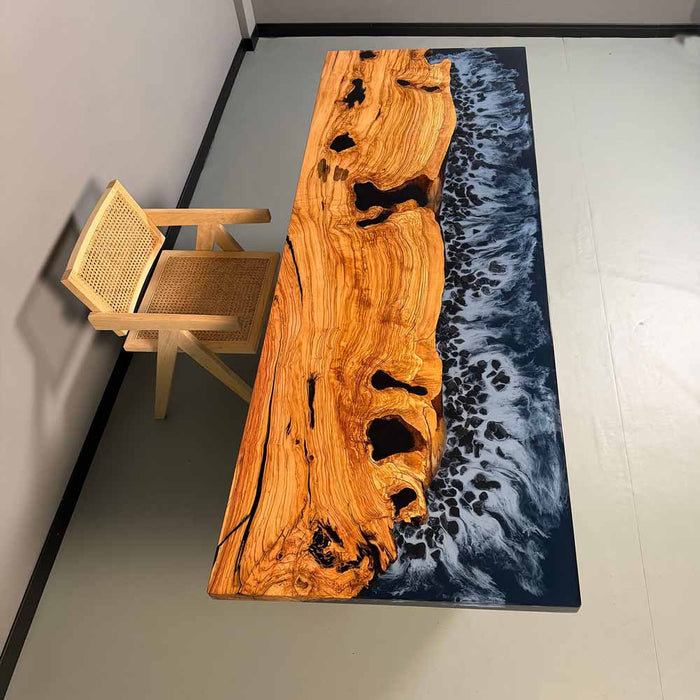 Wooden table with natural grain and black spots, paired with a woven chair on a gray floor.