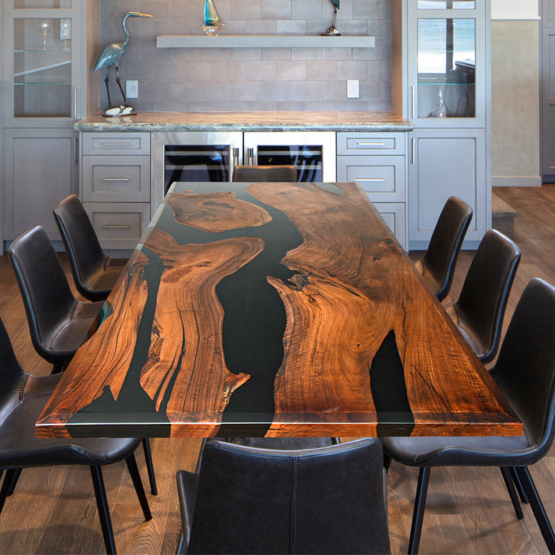 The Custom Black Walnut Epoxy River Table showcases a black walnut live edge slab, seamlessly combined with high-quality epoxy resin to create a stunning contrast. The table top epoxy finish enhances the natural wood grain while providing durability and a glossy shine. Perfect as an epoxy dining table, conference table, or a statement wood and epoxy table for modern interiors. Designed with acrylic legs, this epoxy resin wood table exudes elegance and sophistication. 