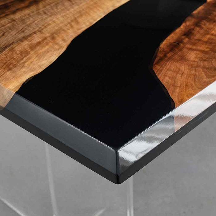 Close-up of a modern coffee table with wooden top, black resin, and glass base.