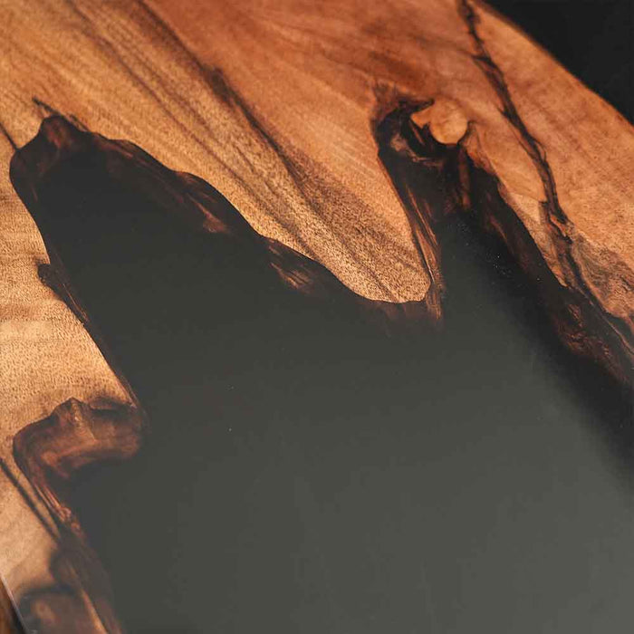 Close-up of a wooden cutting board with a dark liquid pool on a sandy background
