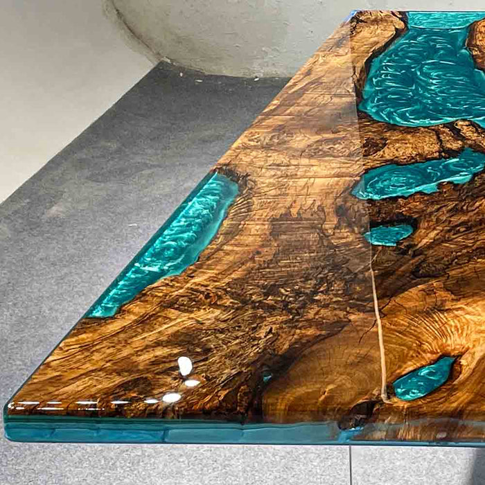 Wooden table with turquoise resin inlays on a gray floor.