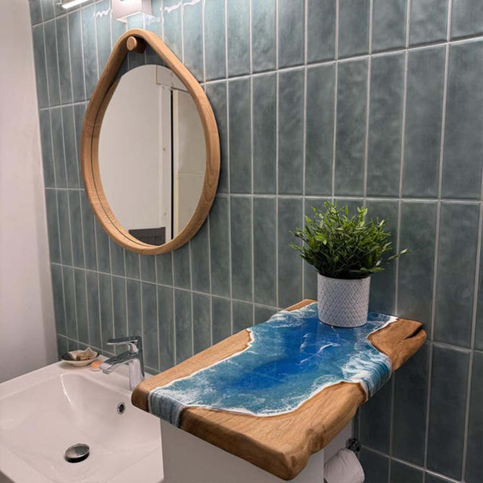 Bathroom with blue tiled walls, a round mirror, and a wooden shelf with a plant.