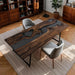 Wooden desk with black glass top in a room with bookshelves and chairs.