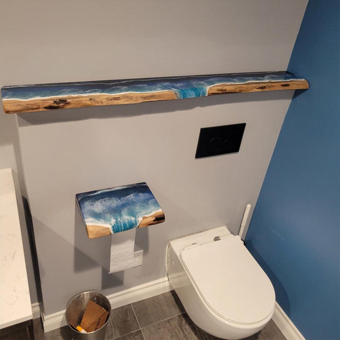 Bathroom with a wooden shelf featuring a resin ocean design, toilet paper holder with similar design, and white toilet.