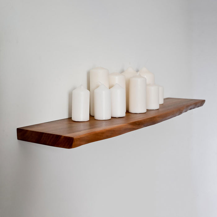 Wooden shelf with white candles on a plain wall
