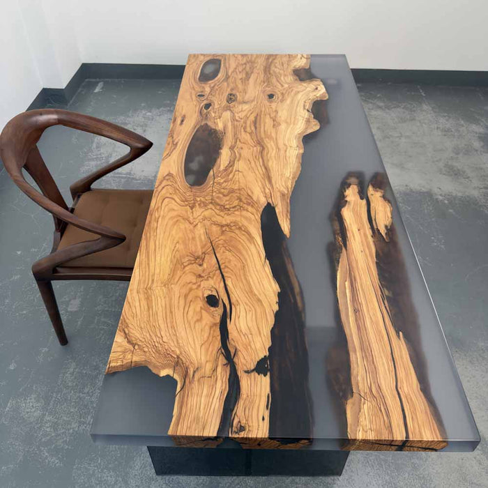 Wooden table with natural grain and black resin accents, paired with a brown chair on a gray floor.