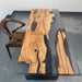 Wooden table with natural grain and black resin accents, paired with a brown chair on a gray floor.