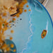 Handcrafted round epoxy resin table with island-inspired artwork and dried flowers in a green vase.