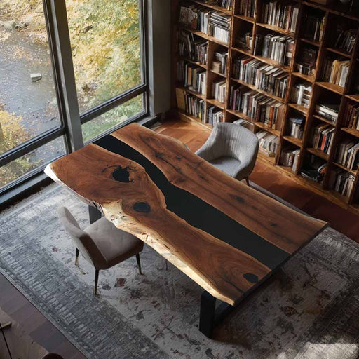 Wooden dining table with black resin accents in a room with bookshelves and large windows.