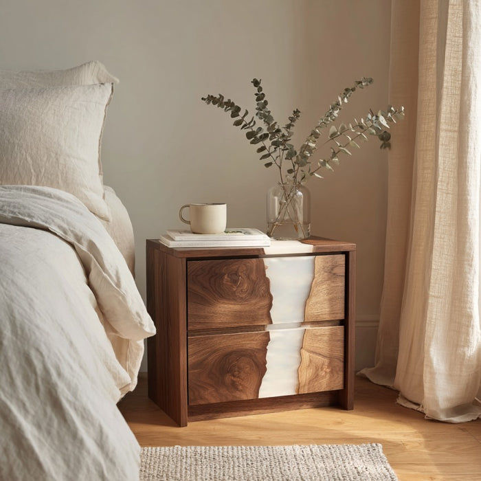 Wooden nightstand with a vase of flowers next to a bed in a bedroom setting.