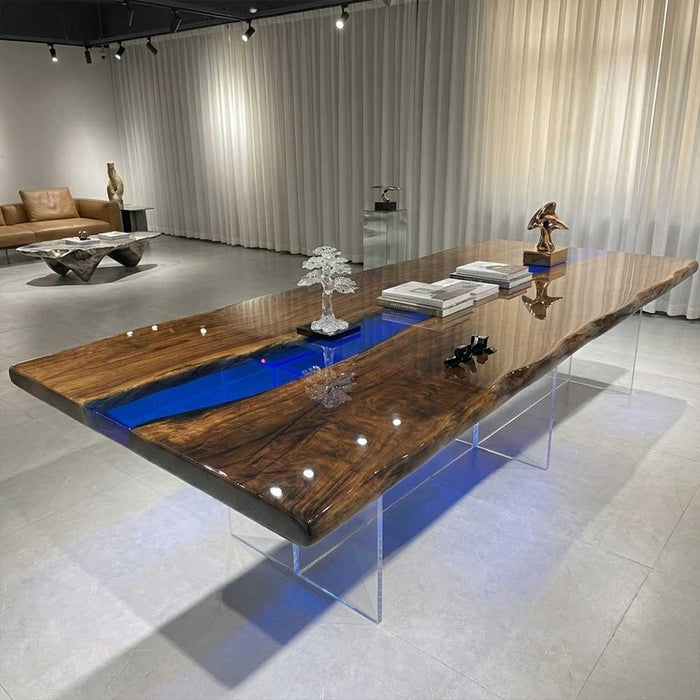 A luxury black walnut dining table with a vibrant ocean blue resin river and clear acrylic legs in a modern showroom.