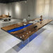 A luxury black walnut dining table with a vibrant ocean blue resin river and clear acrylic legs in a modern showroom.