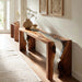 Wooden console table with natural finish in a room with light-colored walls and a rug.