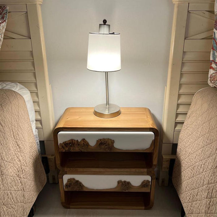 Wooden nightstand with a lamp between two beds in a bedroom setting.