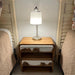 Wooden nightstand with a lamp between two beds in a bedroom setting.
