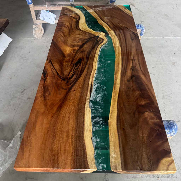 Wooden table with a river-like design of green resin running through it, on a concrete floor.