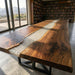 Long wooden table with a river-like design in a room with bookshelves and large windows.