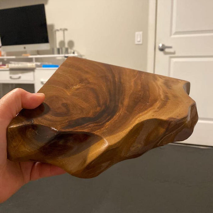 Hand holding a large piece of wood with a wavy edge in an indoor setting