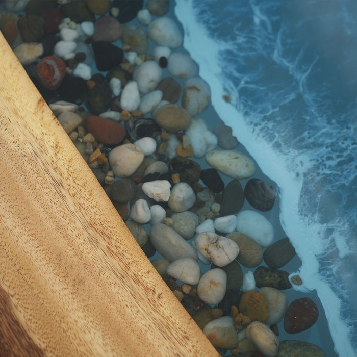 Close-up of pebbles by the ocean with a wooden log partially submerged.