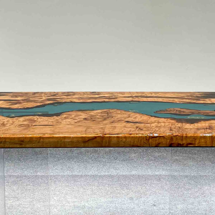 Wooden table with a river-like design of blue material running through it, on a light gray floor.