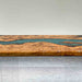 Wooden table with a river-like design of blue material running through it, on a light gray floor.