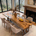 Dining room with a long wooden table and chairs, featuring a fireplace and large windows.