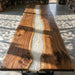 Wooden table with a river of white material running through it, in a room with books and a window.