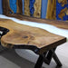 Wooden bench with live edge design and black metal legs against a blue wall.