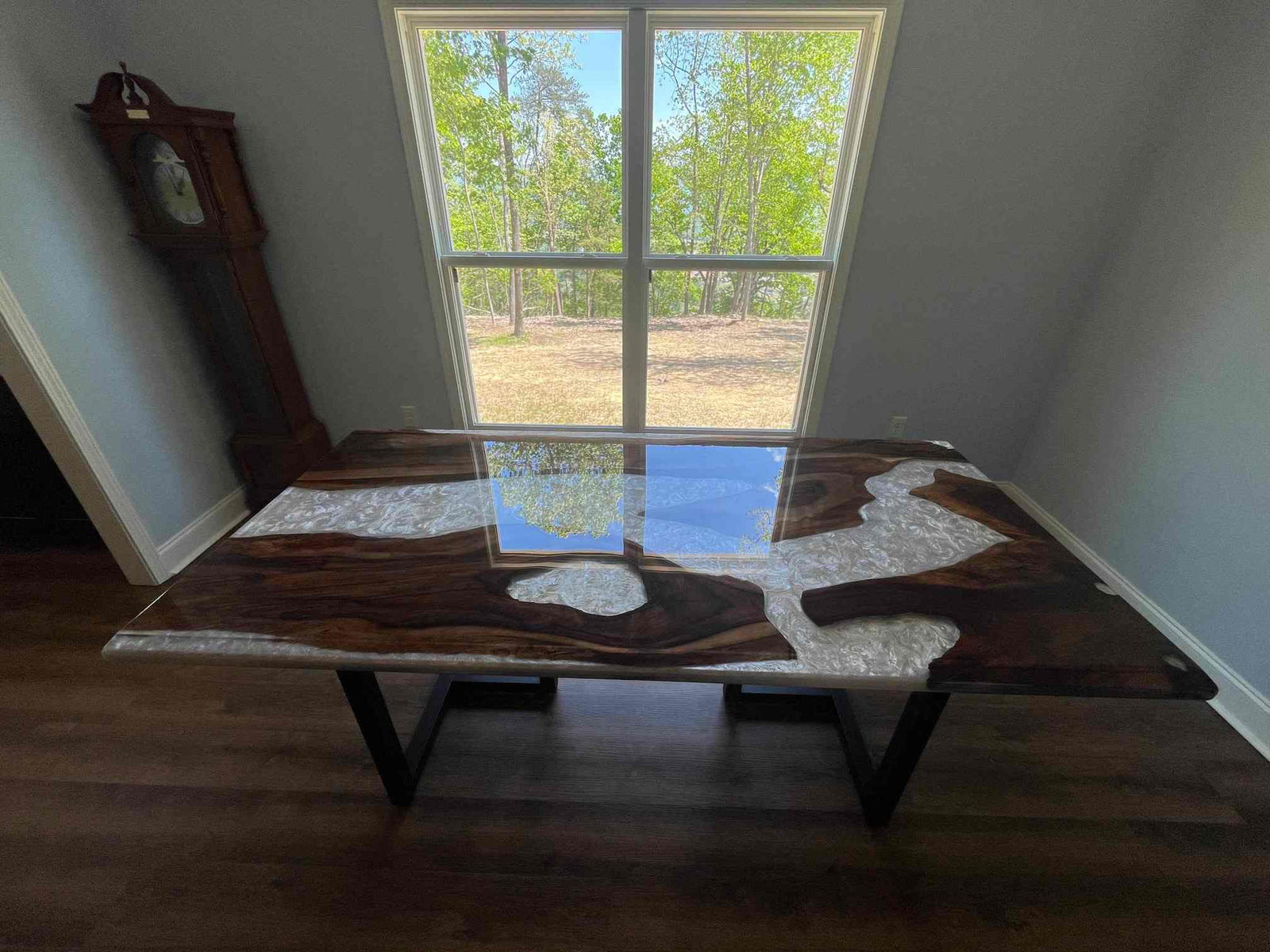 Wooden dining table with a unique design in a room with a window showing trees outside.