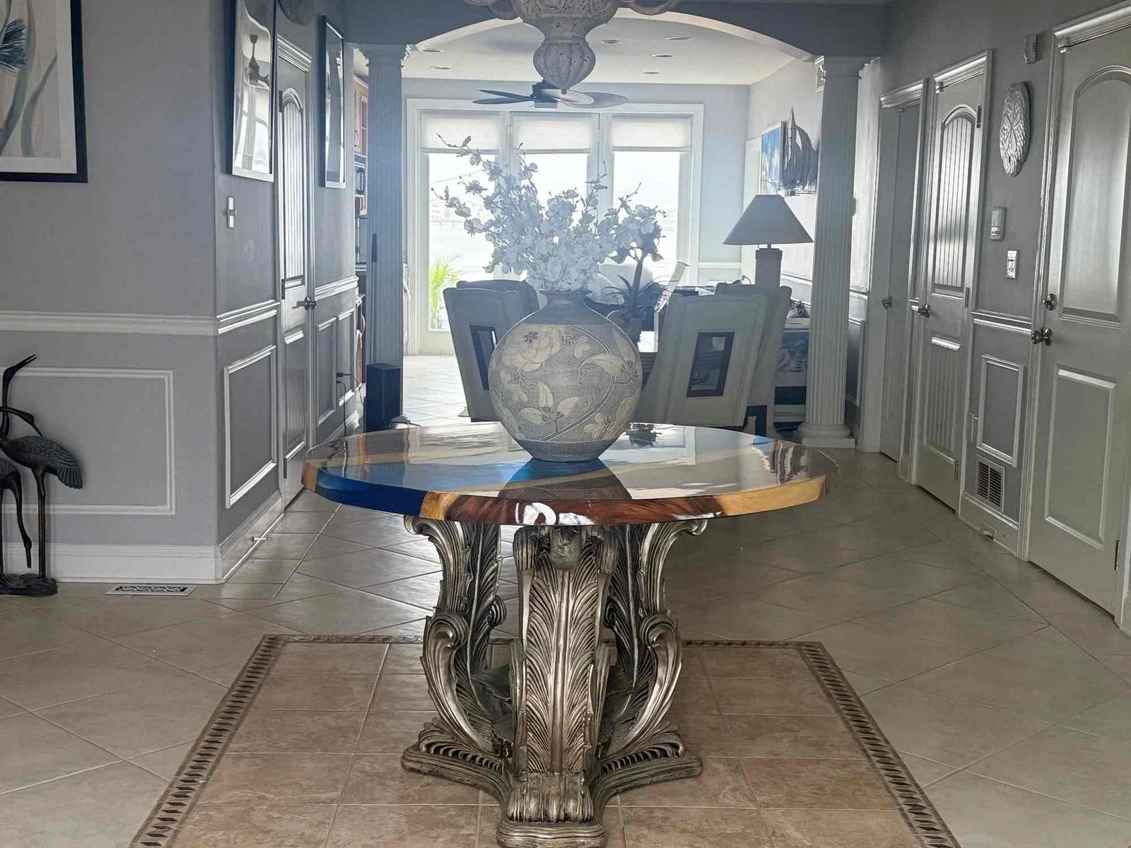 Decorative table with a vase and framed pictures in a room with gray walls and tiled floor.