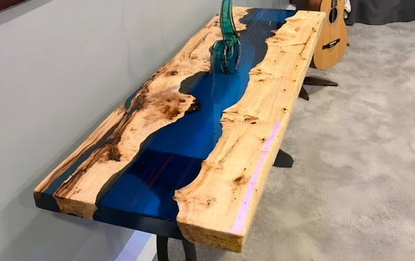 Wooden table with blue resin inlay on a gray floor.
