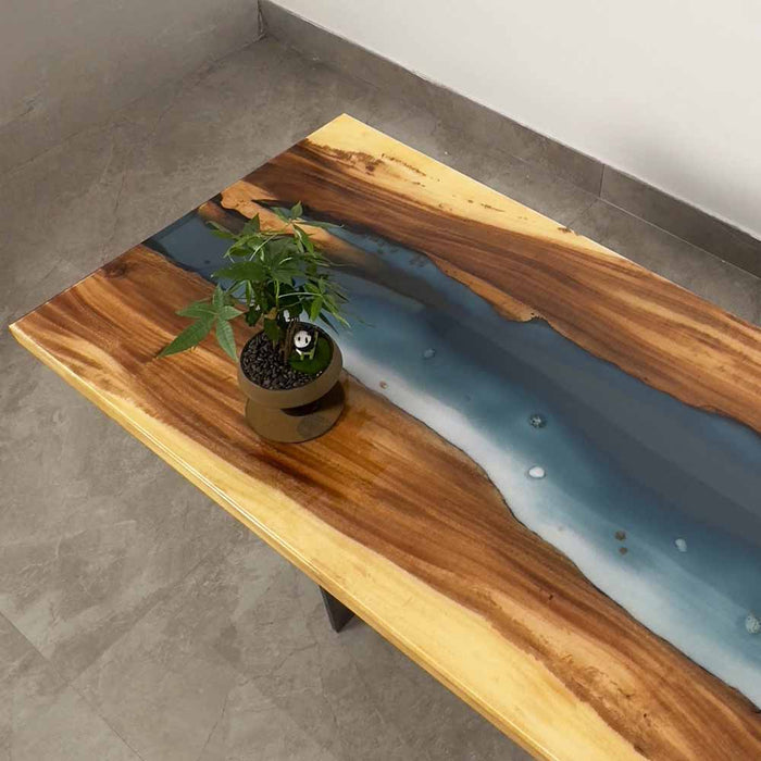 Wooden table with a central blue resin flow and a plant on top, set against a concrete floor.