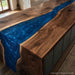 A live-edge wooden kitchen island with a glossy deep blue resin river running through the center, shown in a real indoor kitchen environment.