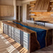 A large kitchen island with a glossy dark wood top and a vivid blue resin river running through the center, set in a modern kitchen with wood cabinetry and backsplash.