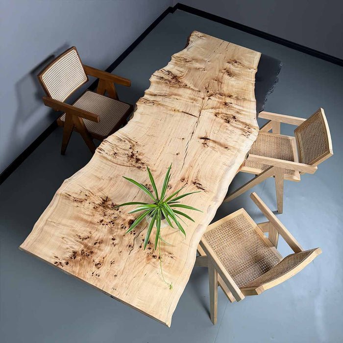 Wooden dining table with natural finish and three chairs on a gray floor.