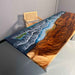 Wooden table with a scenic design of waves and land, placed against a plain wall.