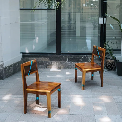 Two wooden chairs with blue accents on a tiled pavement outside a building.
