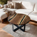 Round wooden coffee table with black metal legs in a living room setting.
