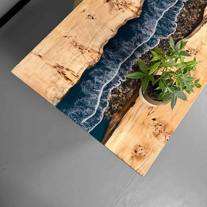 Wooden table with live edge design and embedded blue resin, featuring a potted plant on a gray surface.