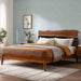 Wooden bed in a bedroom with a light blue wall and framed picture.