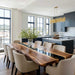 Modern kitchen with a long wooden dining table and chairs, featuring a large window view.