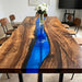 Coastal inspired artisan furniture featuring a bright blue resin river table styled with decorative books and sculptures.