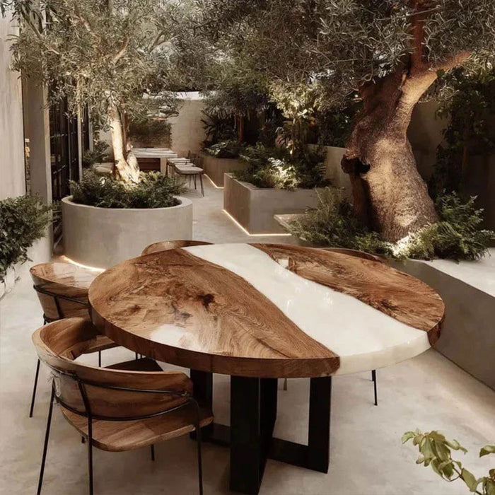 Wooden dining table with white top in an outdoor setting with trees and plants.