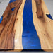 Wooden table with blue resin inlay on a gray floor.