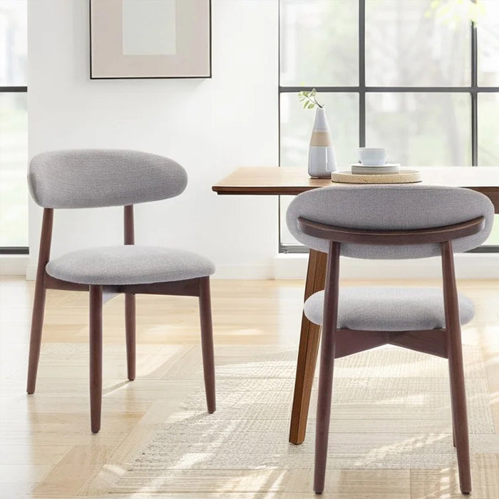 Two gray cushioned chairs with wooden legs in a bright room.