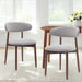 Two gray chairs with wooden legs in a bright room with a table and flowers.