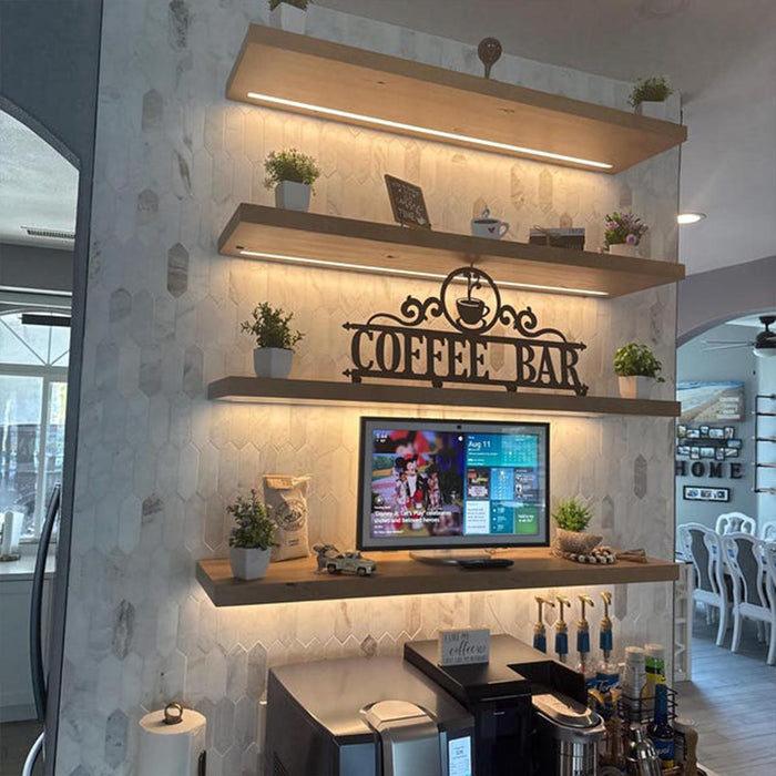 Coffee bar setup with a television screen displaying menu options, surrounded by shelves with plants and decor.
