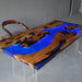 Wooden table with blue resin inlay and clear legs on a gray floor.